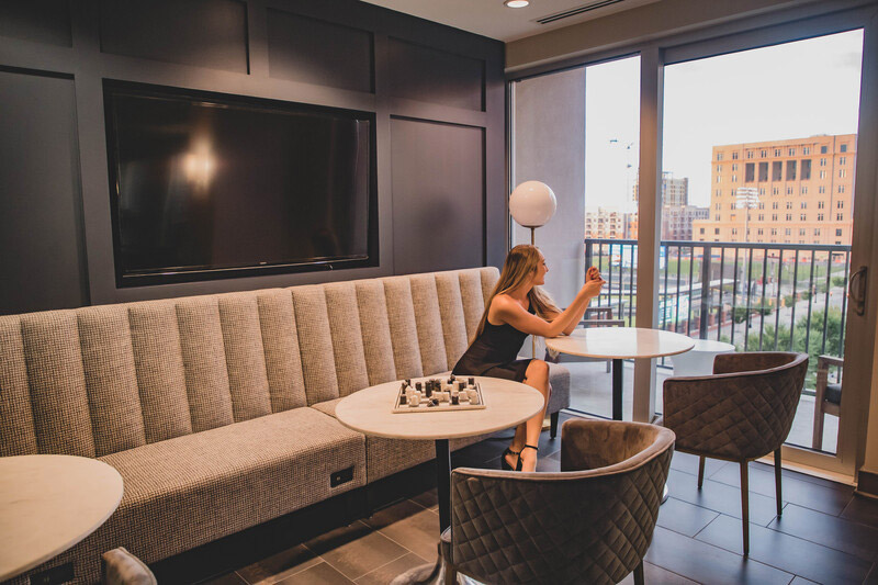 Woman sitting in clubhouse with bench style seating, flat screen TV and large windows overlooking downtown