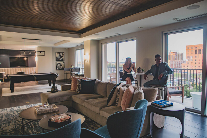 Couple hanging out in a clubhouse with plush seating, bistro seating, pool table, large windows with a view and flat screen TV